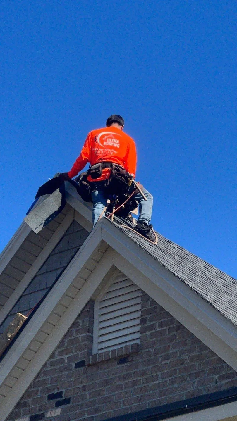 Ultra Roofing crew member in an orange shirt working on a roof ridge against a blue sky