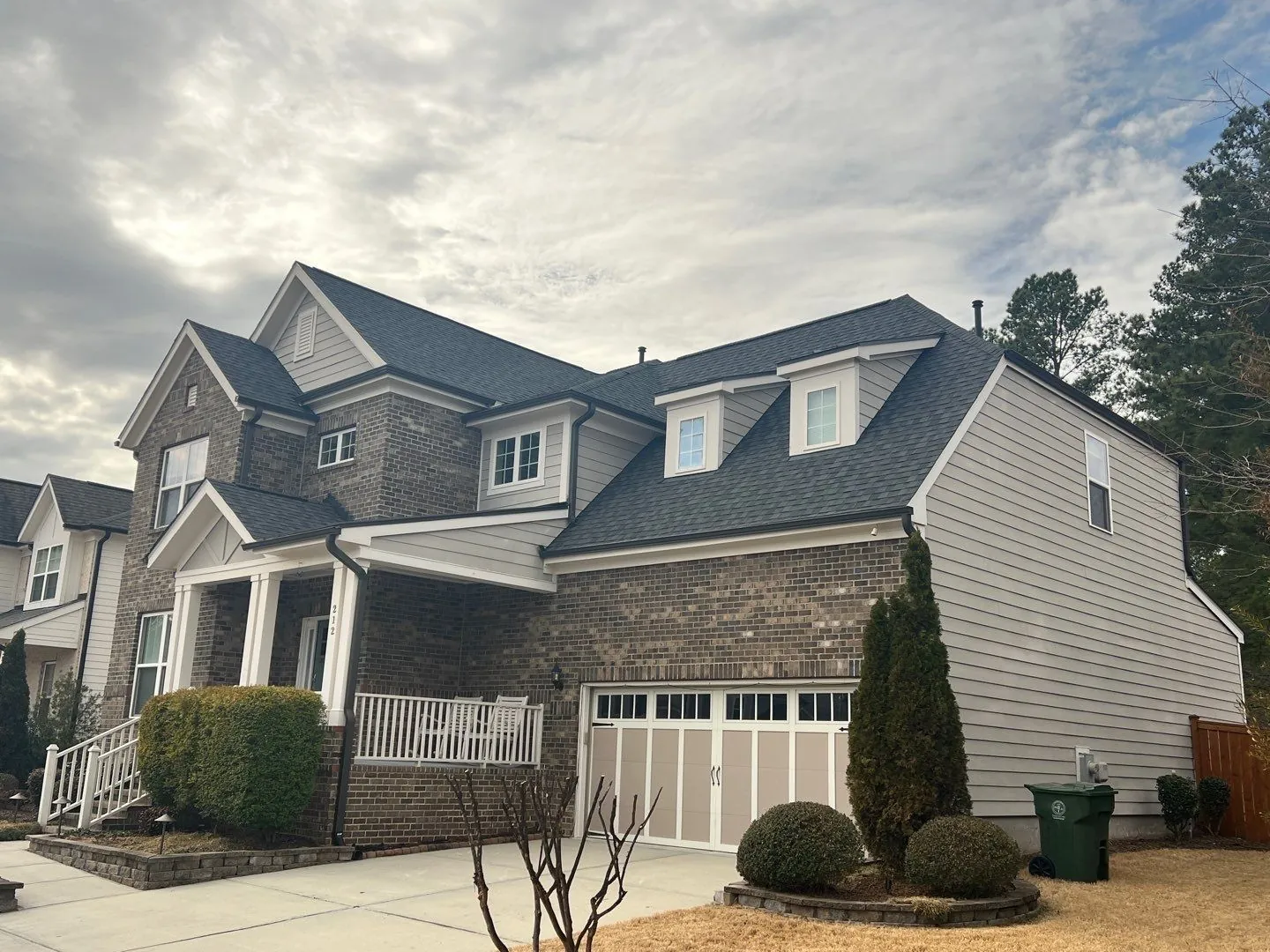 Two-story brick and siding home with a dark shingle roof under a cloudy sky