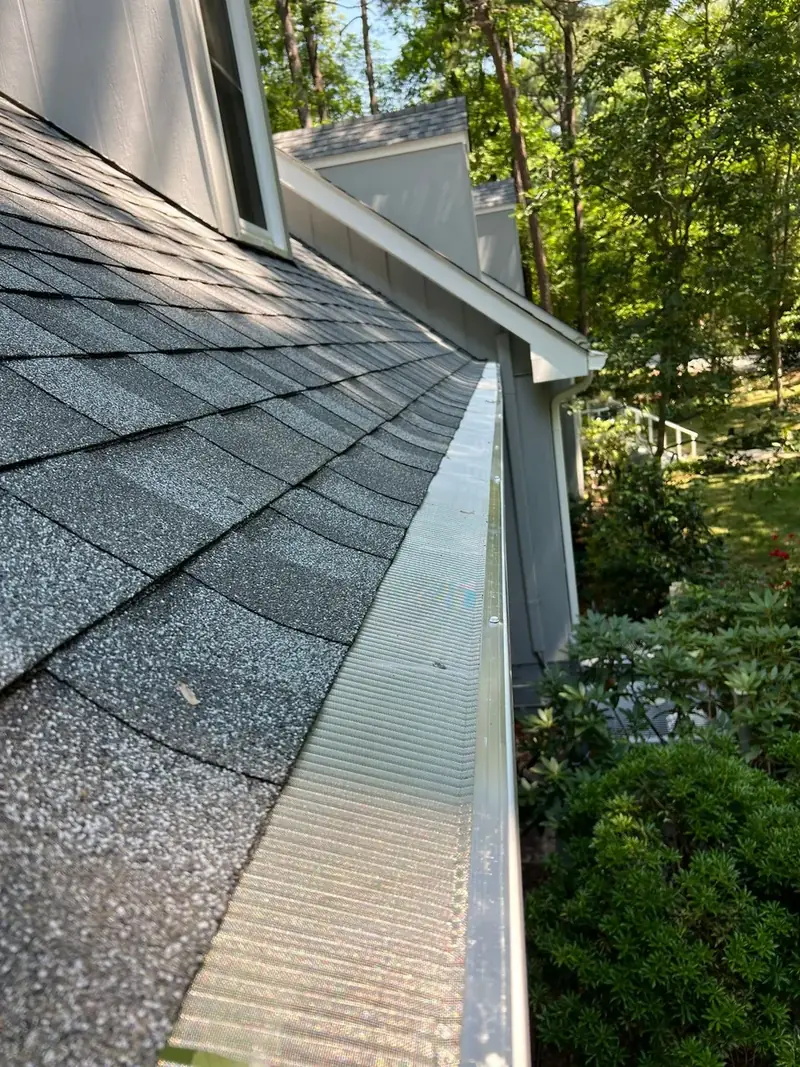 Close-up of a white gutter with a mesh gutter guard along a shingle roof edge