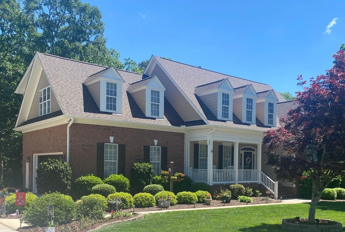 Brick home with a newly installed brown architectural shingle roof and two dormers