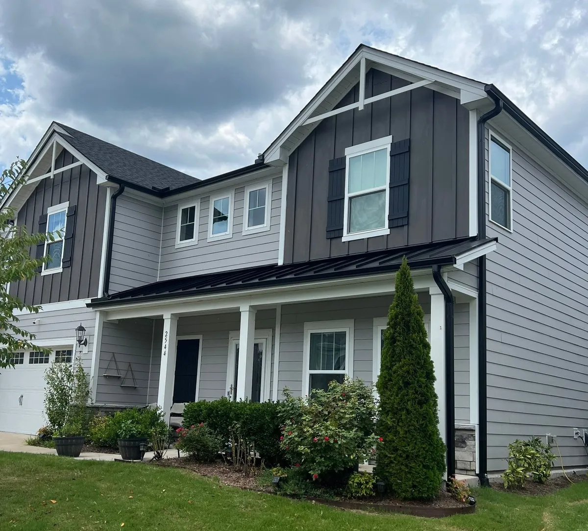 Two-story home with gray board-and-batten and lap siding and a black metal porch roof